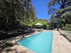 A rectangular swimming pool with a tiled deck, surrounded by a fence and trees. - Breathtaking house in Crafers West - sleeps 10 (Crafers West)