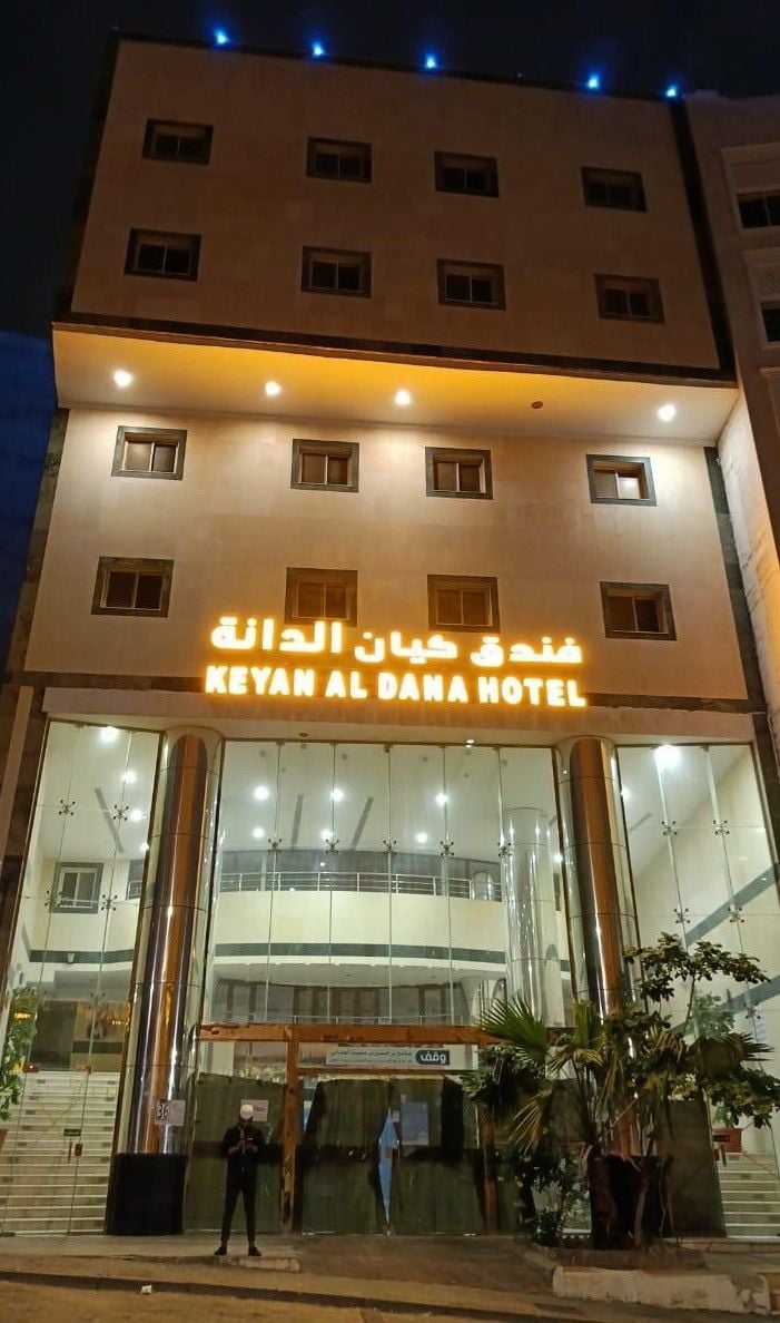 A hotel with a sign in Arabic and English, multiple floors, and a glass facade.