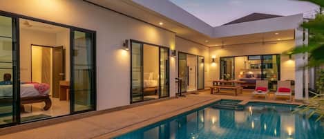 Un hotel moderno con piscina, puertas de vidrio que dan a las habitaciones y un patio con mobiliario.