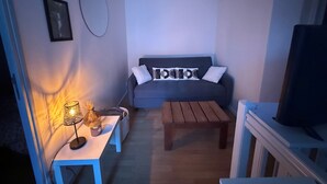 Ein Wohnzimmer mit einer Couch, einem Couchtisch, einem Fernseher, einer Lampe und einem gerahmten Bild an der Wand.