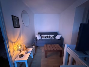 Een woonkamer met een bank, een salontafel, een televisie, een lamp en een lijst met een afbeelding aan de muur.