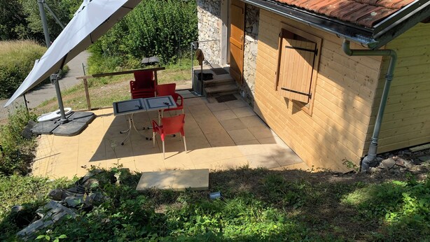 Eine kleine Außenpatio mit Tisch und Stühlen, einem überdachten Bereich und einem Gebäude mit einem Ziegeldach.
