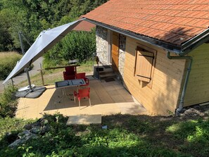 A small outdoor patio with a table and chairs, a covered area with a white canopy, and a stone wall adjacent to a wooden building with a tiled roof. - Cozy chalet for 2 to 4 people—20 minutes from Chamonix (Passy)