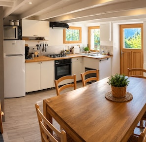 Een keuken met een houten tafel, stoelen, een fornuis, oven, magnetron en kastjes.