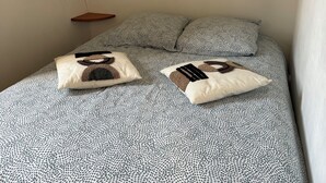 Ein Bett mit gemustertem Bettbezug und zwei Kissen, ein Nachttisch und eine wandmontierte Leuchte.