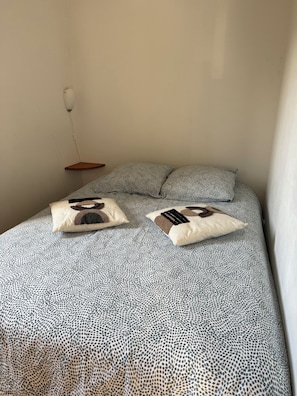 Een bed met een gebedruid sprei en twee kussens, een nachtkastje en een wandlamp.