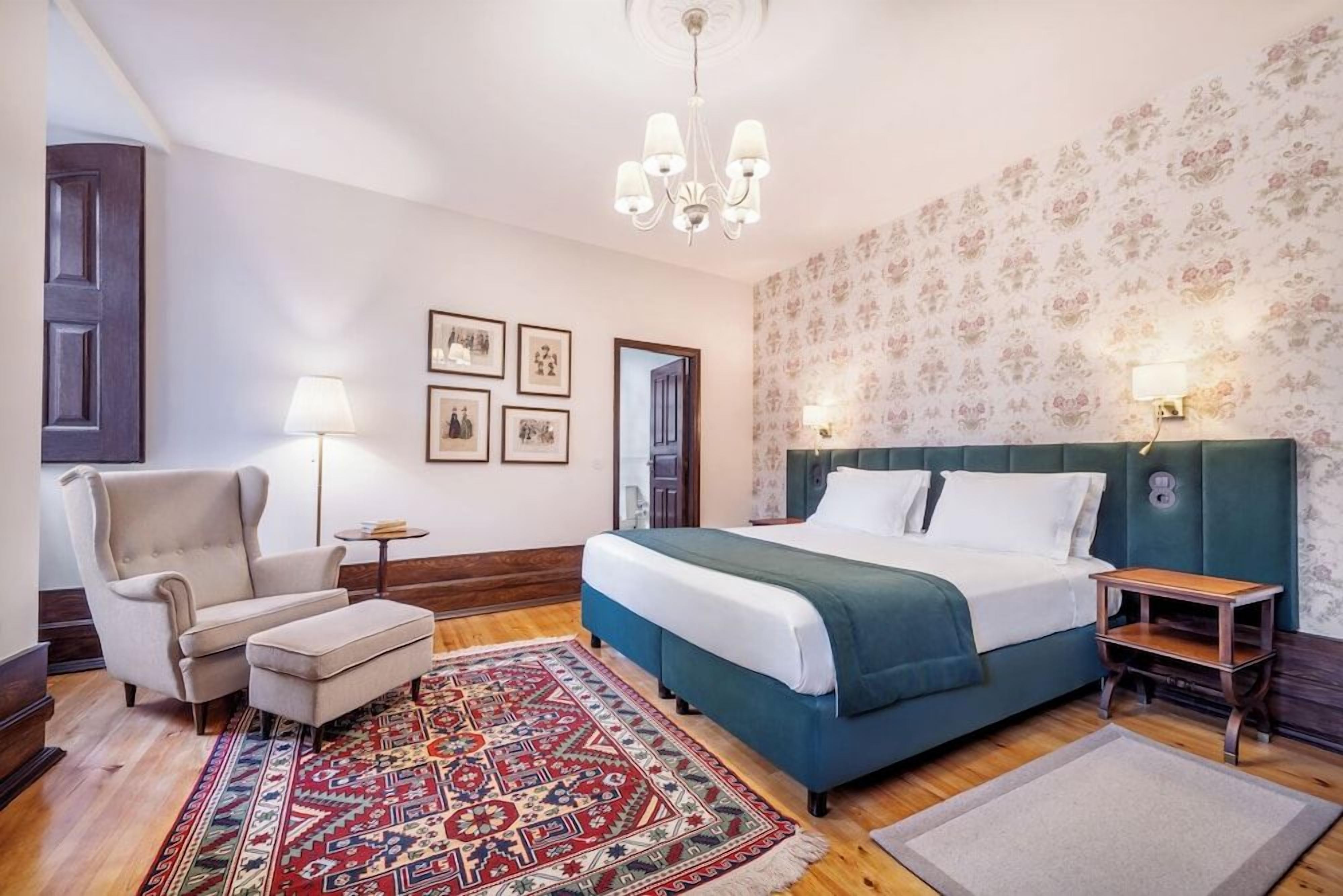 A bedroom with a bed, a chair, a rug, and a nightstand.