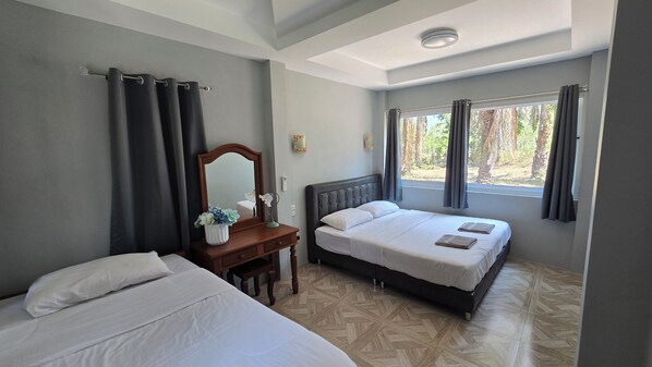 A bedroom with two beds, a wooden dresser, a mirror, and a window with curtains.