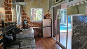 A compact kitchen with a refrigerator, a window, and a view of a swimming pool.
