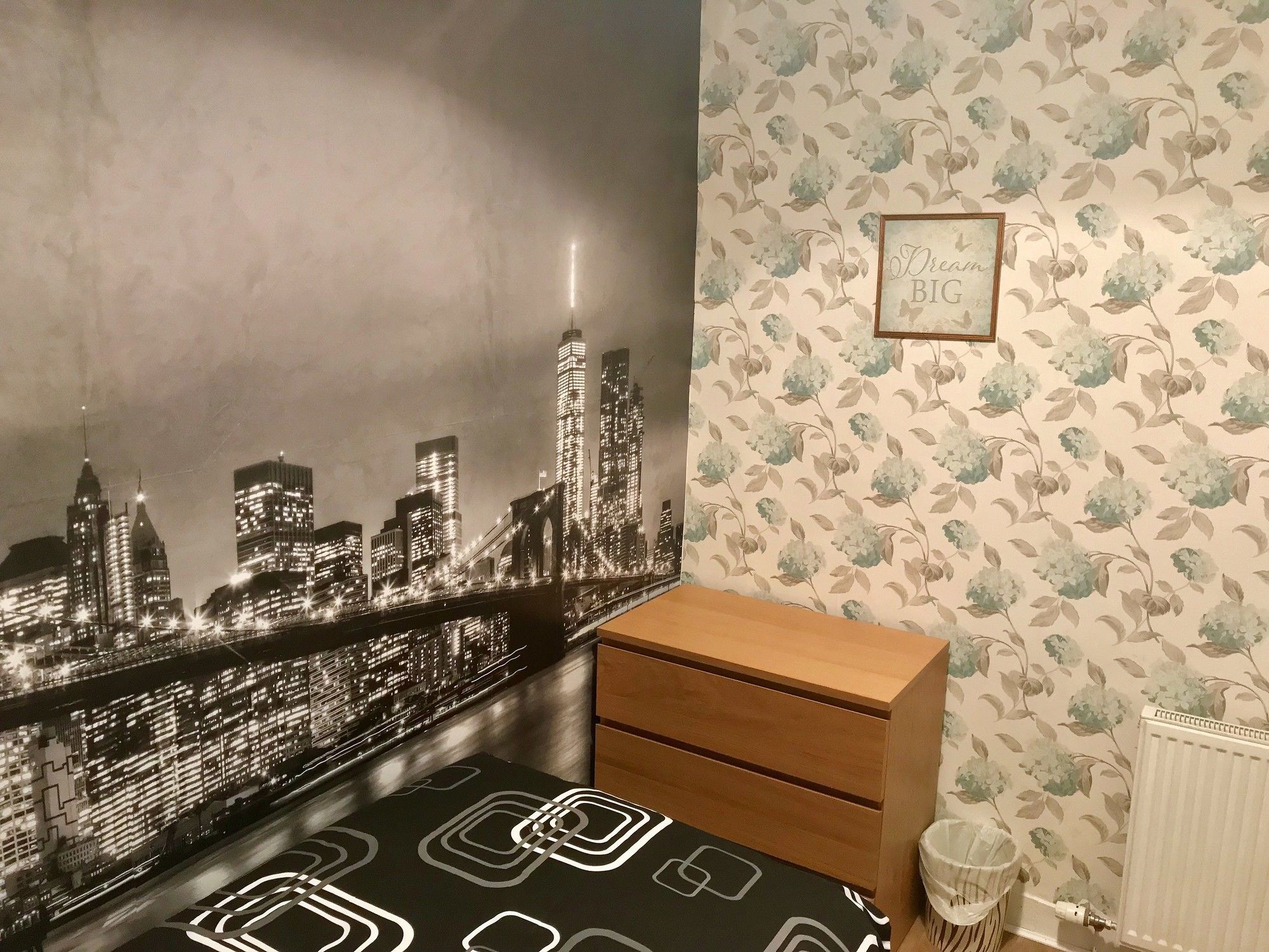 A room with a cityscape mural, a radiator, and a framed inspirational quote on the wall.