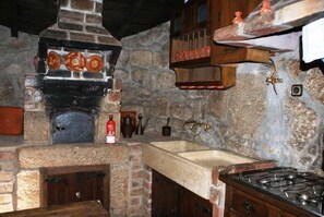 Une cuisine rustique avec un mur en pierre, un poêle à bois, un évier et un étendoir suspendu.