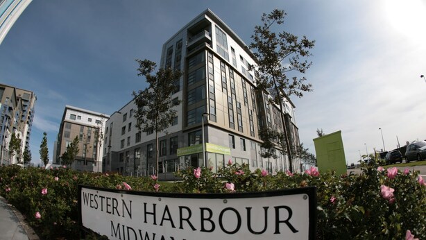 Une enseigne indiquant « Western Harbour Midway », avec des bâtiments modernes en arrière-plan.