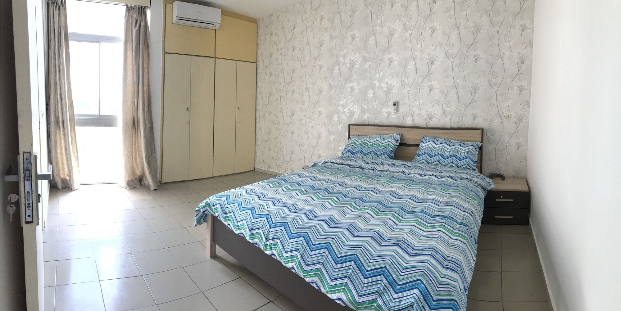 A bedroom with a bed, nightstands, a wardrobe, and an air conditioning unit.
