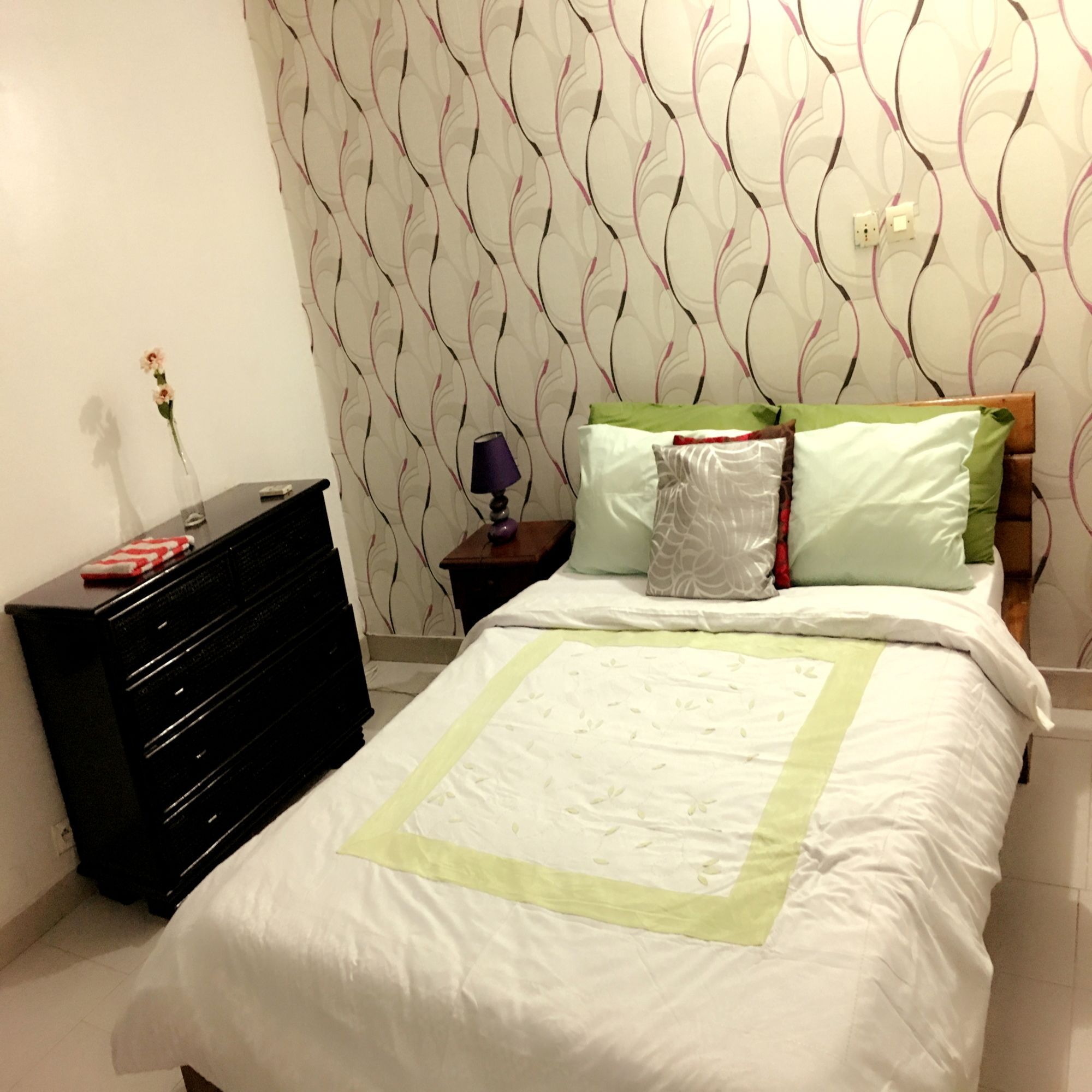 Un dormitorio con cama, cómoda, mesita de noche y una pared con estampado de hojas.
