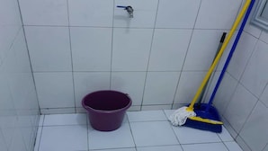 Ein kleines Badezimmer mit Fliesen, einem violetten Eimer, einem Mopp und einem Duschkopf.