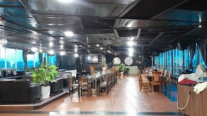 Un restaurant amb una barra llarga, diverses taules i vistes a la ciutat a través de grans finestres.
