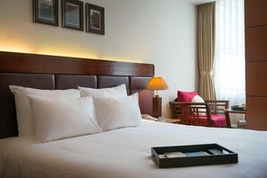 Ein Hotelzimmer mit einem großen Bett, einem Nachttisch mit Lampe, einem Sessel und einem kleinen Tisch mit Telefon.