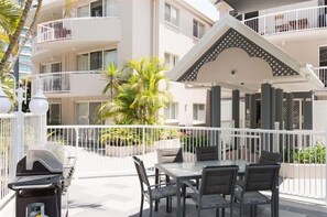 Un patio exterior con mesa y sillas, una parrilla y un edificio con balcones al fondo.