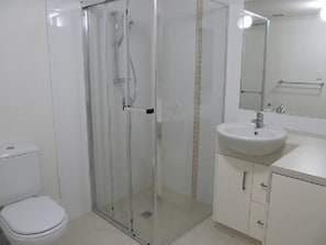 Un baño con ducha acristalada, lavamanos blanco y retrete.