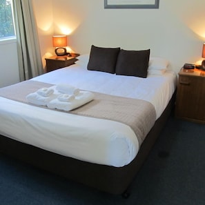 Una habitación de hotel con una cama grande, dos mesitas de noche y una ventana con cortinas.