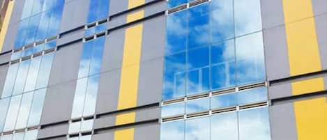 A multi-story building with a glass facade reflecting the sky and clouds.