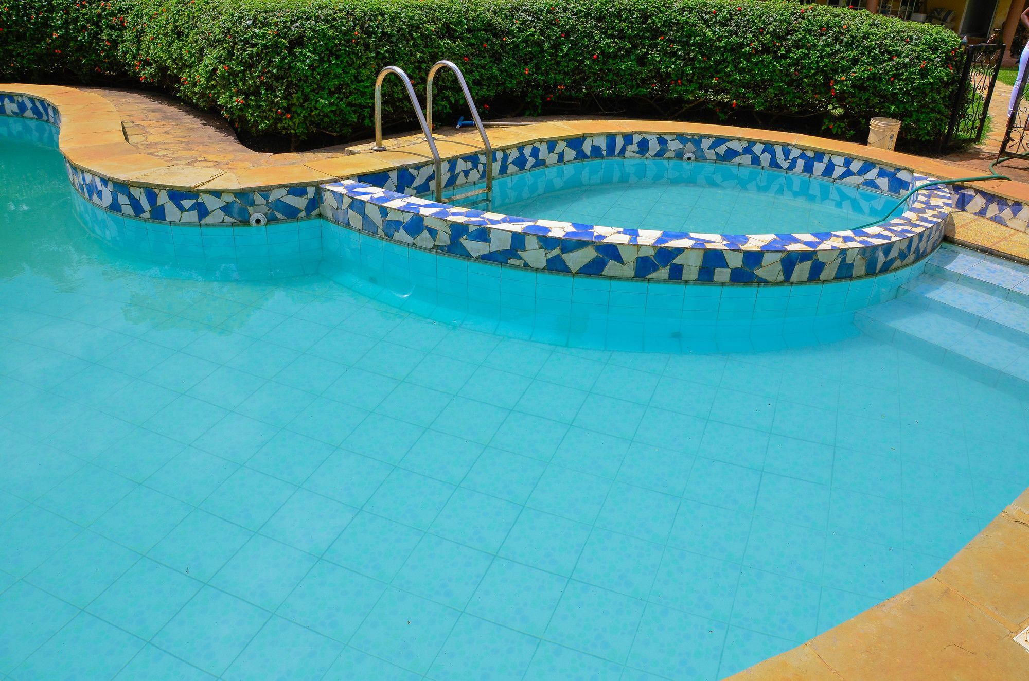 Uma piscina com borda revestida em azulejo e escada de metal.