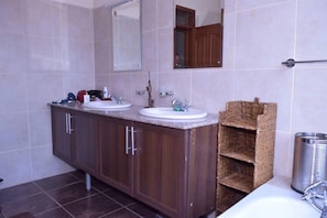 A bathroom with two sinks, a mirror, and a wooden shelf. - Ringsview (Barsaloi)