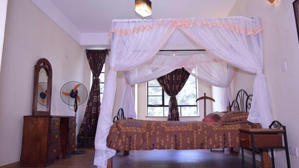 Quarto com cama sob um dossel, penteadeira de madeira, ventilador e janela com cortinas.
