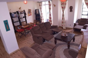 A living room with brown sofas, a wooden coffee table, and a red dining table. - Ringsview (Barsaloi)