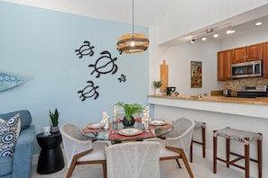 Eine moderne Küche mit Essbereich, ausgestattet mit einer hellblauen Wand, einer Pendelleuchte und einem Holzer Schneidebrett.