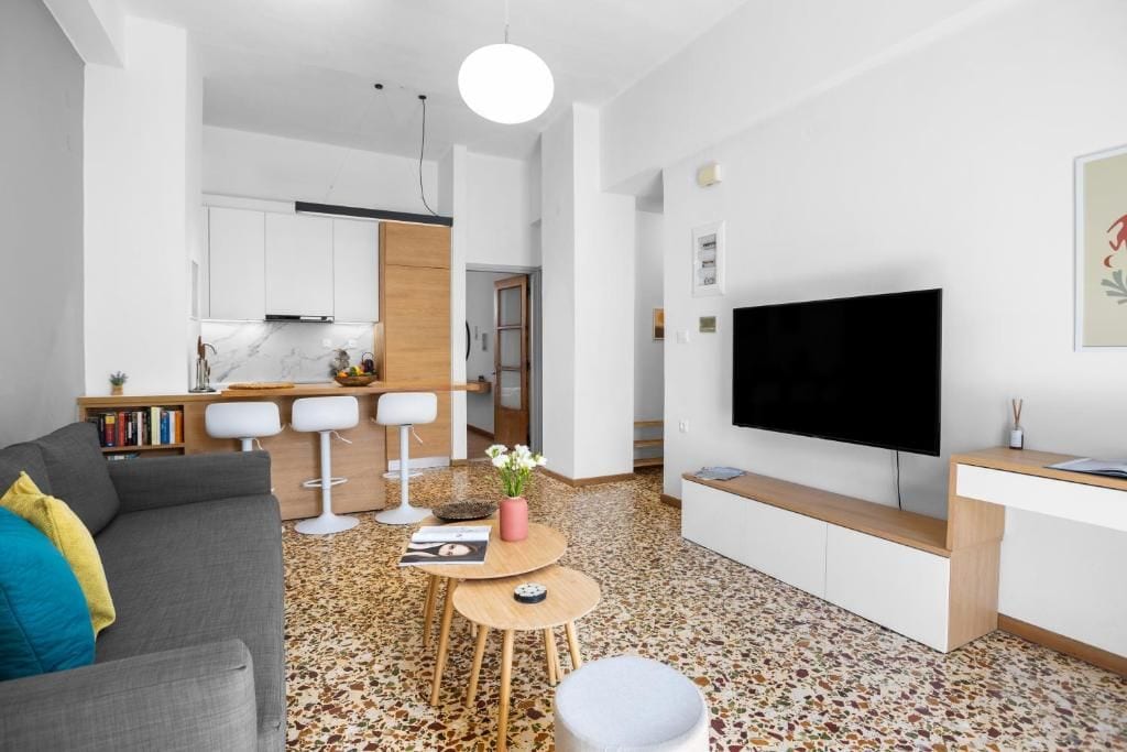 Un salon moderne avec un canapé gris, un téléviseur à écran plat et une cuisine en arrière-plan.