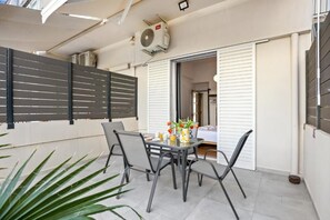 An outdoor patio with a table and chairs, a potted plant, and a sliding door leading to a room. - Renovated Apartment in Central Chania | 5 Min from the Old Town & Port | Spacious Terrace (Chania)