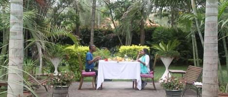 Un jardín con mesa y sillas, rodeado de palmeras y plantas en macetas.