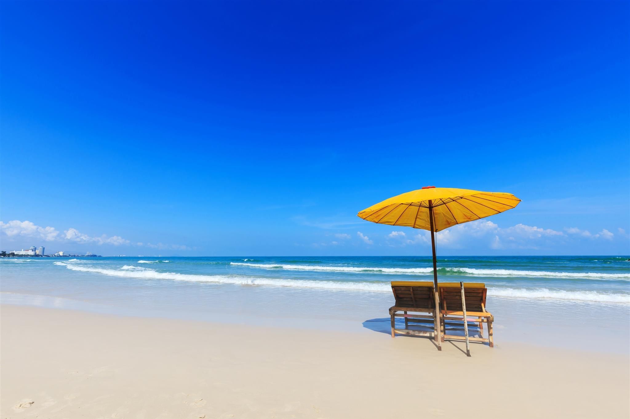 Escena de playa con un banco de madera y un paraguas amarillo.