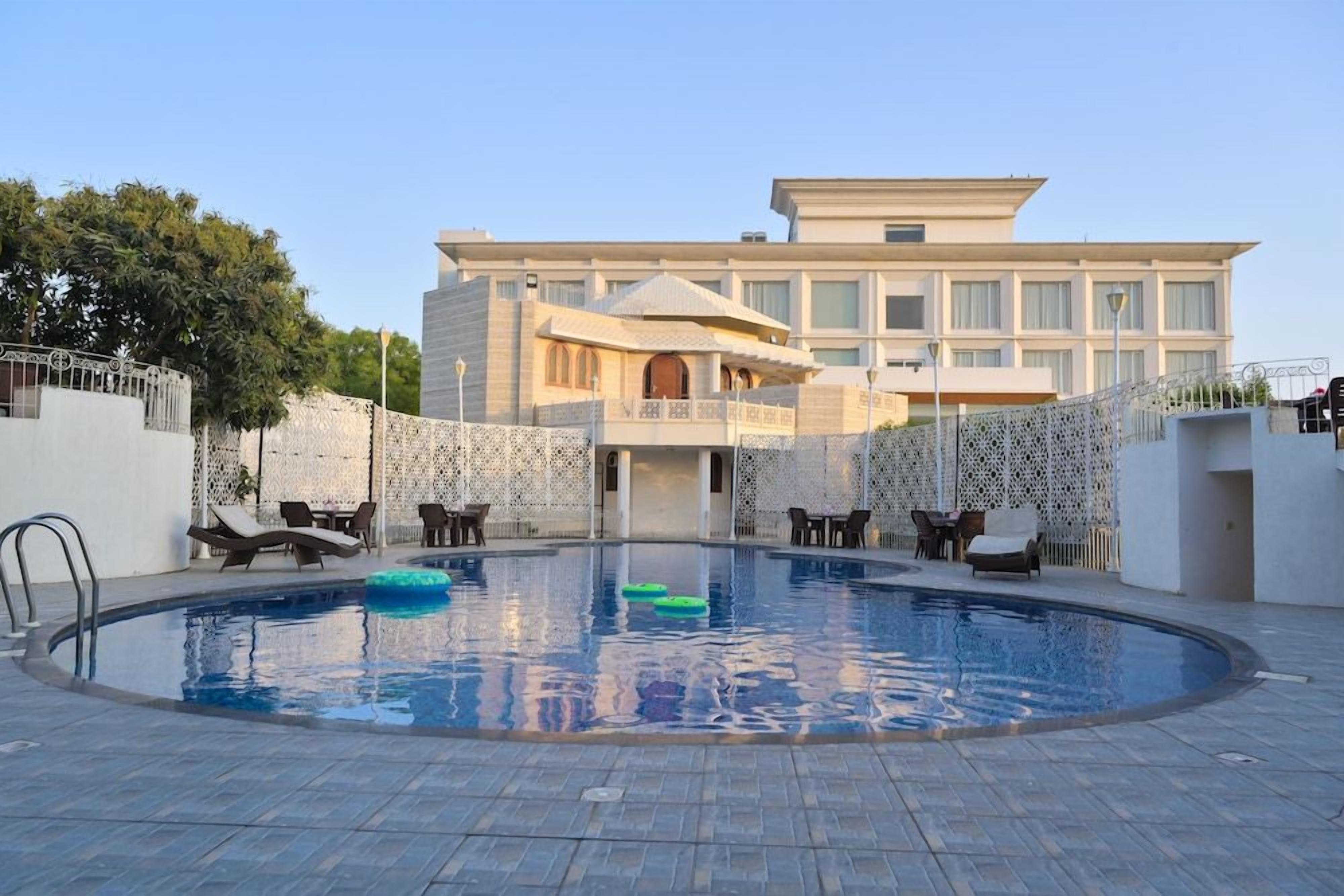Una piscina con sillones de descanso y un edificio al fondo.