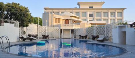 Una piscina con sillones de descanso y un edificio al fondo.