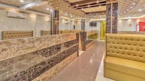Un hall de hotel con suelo de mármol, asientos acolchados y un diseño de techo con motivos.