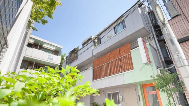 A multi-story building with balconies, a door with a sign, and some greenery in the foreground. - Akasaka-no Sato Female Only (Tokyo)