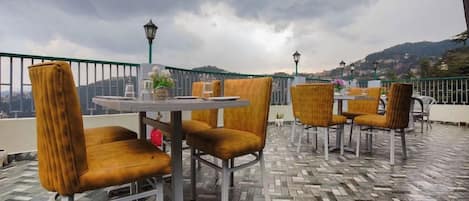 Un espacio al aire libre con mesas y sillas redondas, un suelo con diseño y vistas a un paisaje urbano.