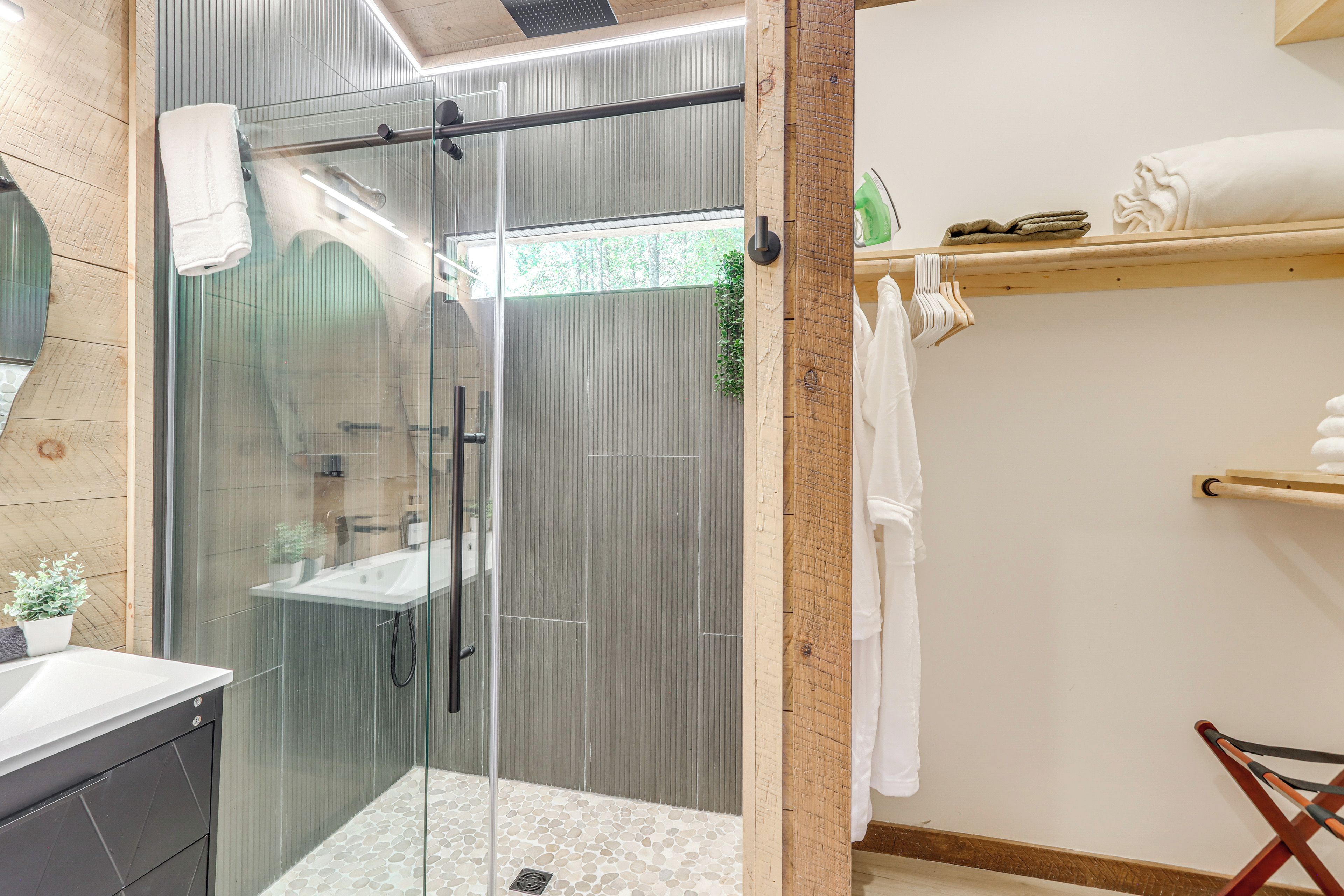 Un baño moderno con cabina de ducha de vidrio, tocador de madera y estante con toallas dobladas.