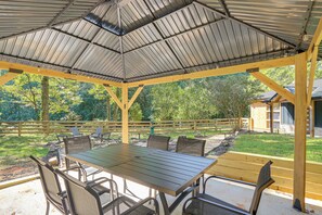 Eine überdachte Terrasse im Freien mit Tisch und Stühlen, umgeben von einem Holzzaun und Bäumen.