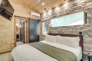 Un dormitorio con cama, pared de piedra, techo de madera y puerta corredera.