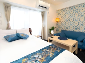 A hotel room with a bed, a sofa, a small table, and a wall-mounted air conditioner.