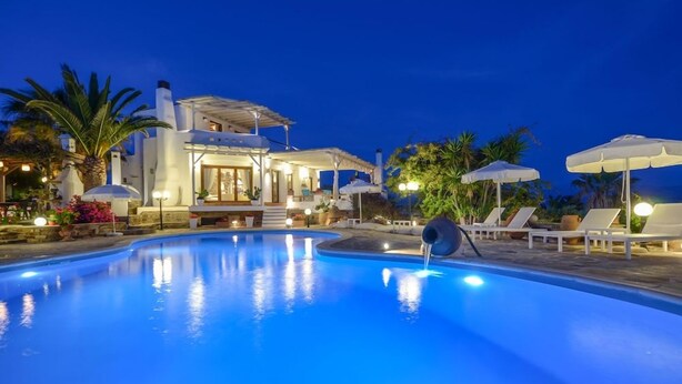 A swimming pool with a water feature, lounge chairs, umbrellas, and a building with a covered patio area. - Villa Pari Manda (Naxos)