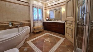 A spacious bathroom with a large bathtub, a separate shower area, and a vanity with a mirror. - Villa Pari Manda (Naxos)