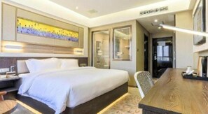 Ein Hotelzimmer mit einem großen Bett, einem Schreibtisch und einem Stuhl. Ein großes Fenster und eine Tür zum Badezimmer sind ebenfalls vorhanden.