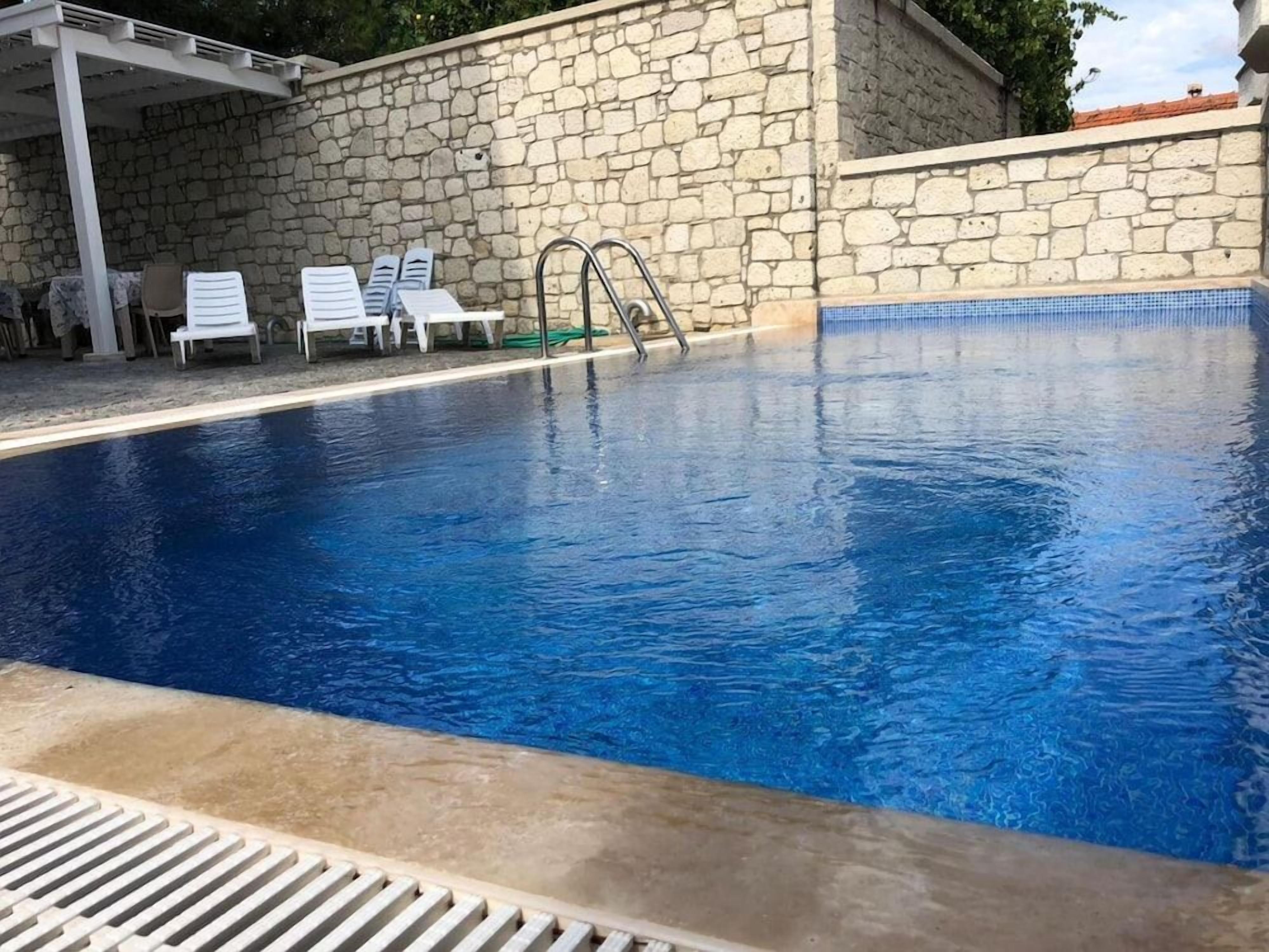 A swimming pool with a stone wall, lounge chairs, and a covered seating area.