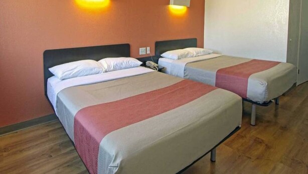Habitación de hotel con dos camas, cada una con cabecera, mesita de noche y lámpara de pared.