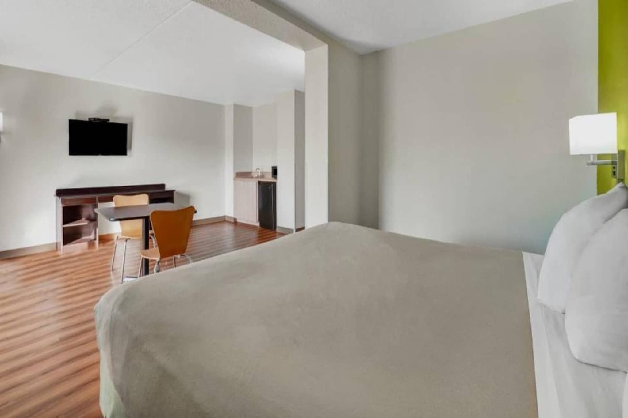 Una camera d'albergo con un letto, una scrivania, una sedia e un televisore appeso al muro.