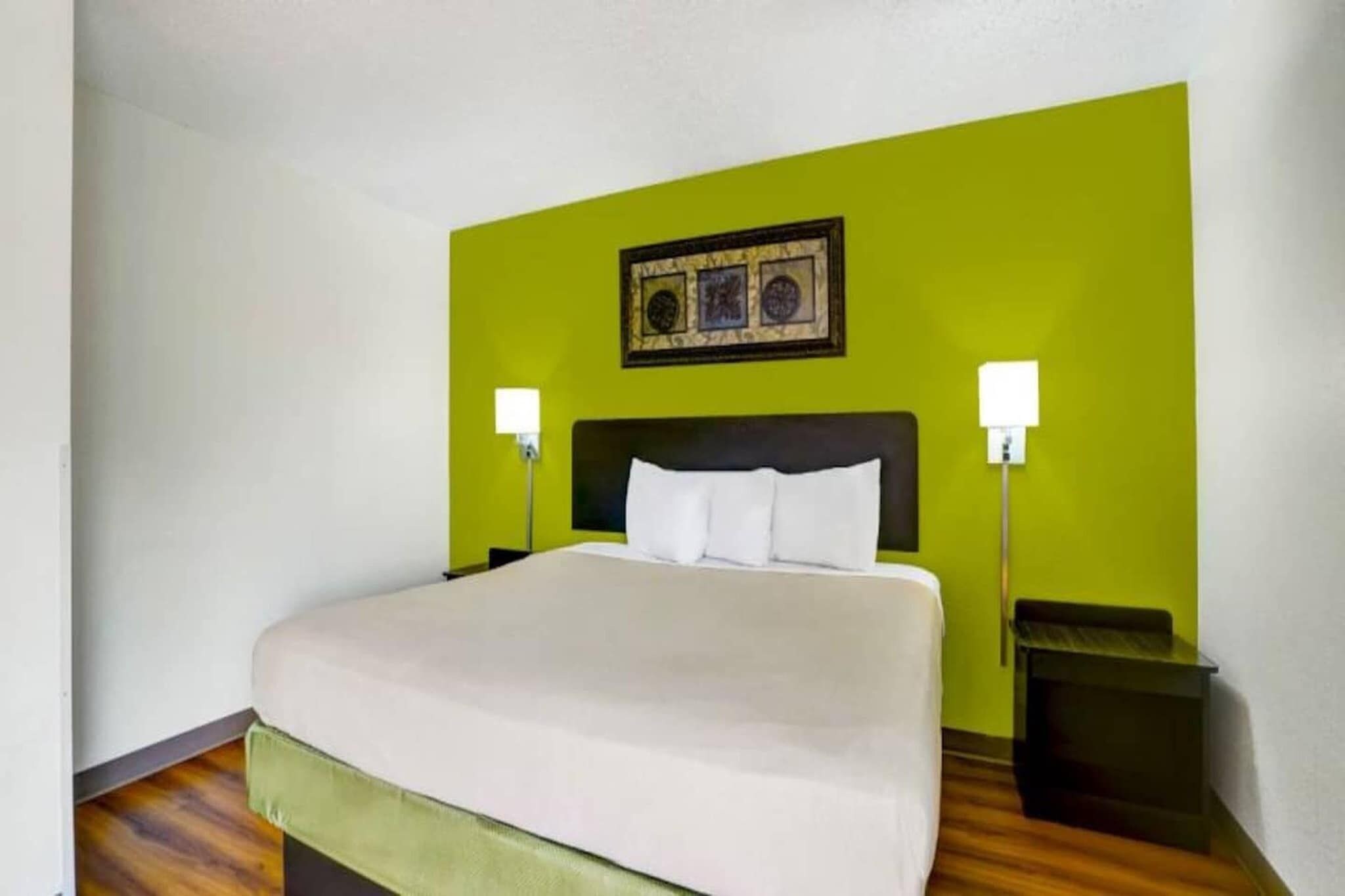 Quarto de hotel com uma cama grande, duas luminárias de cabeceira e uma obra de arte emoldurada acima da cama.